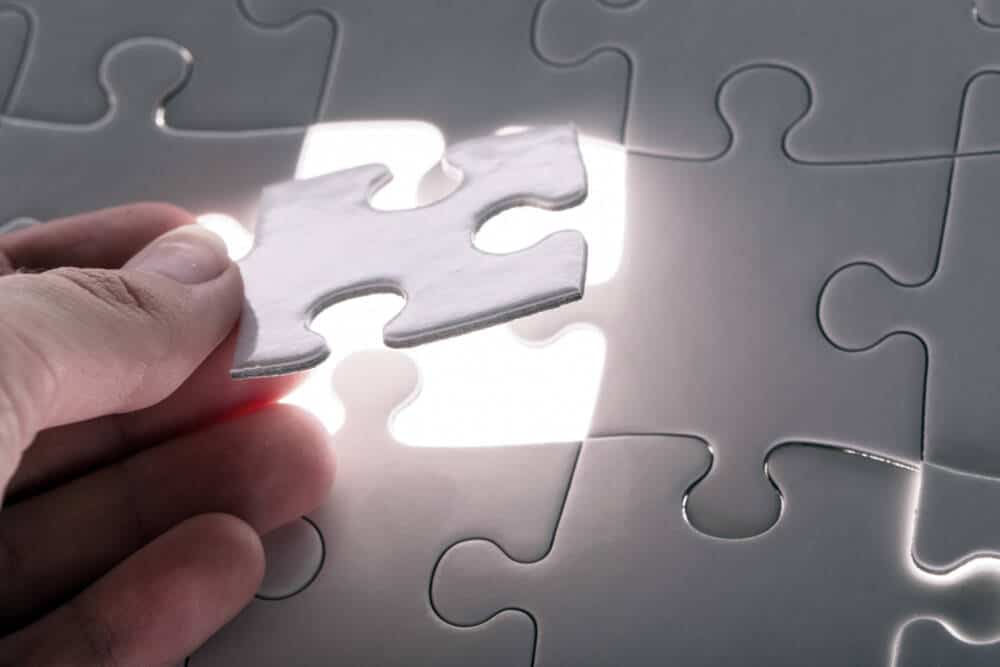 Hand laying the last piece of a luminous white puzzle