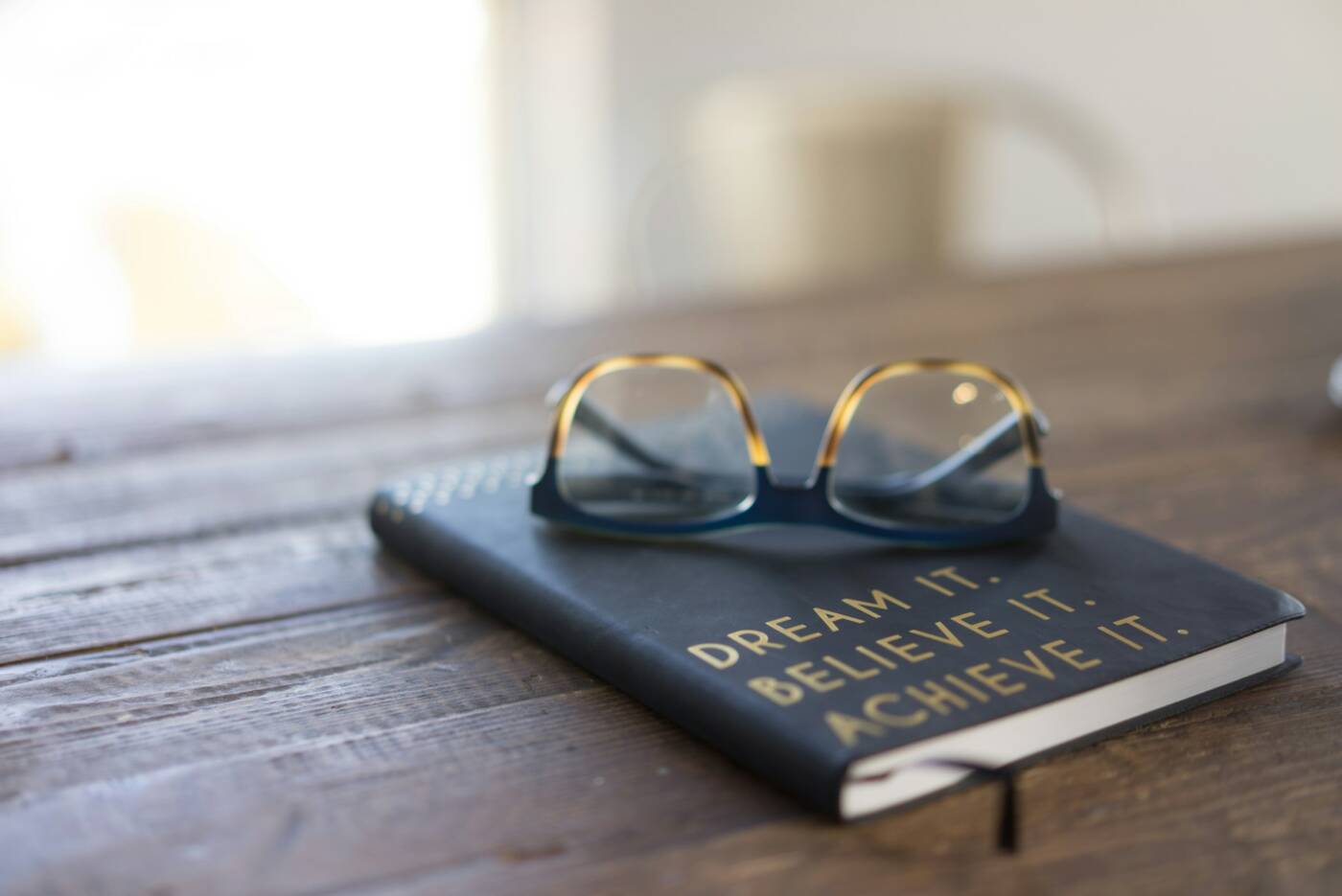 A book on a wooden table with glasses on it. The cover reads 